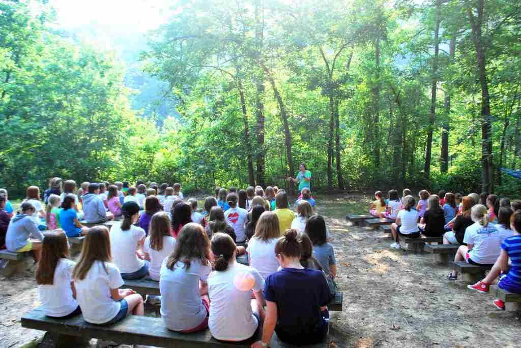 Campers seated on benches in the woods listening during Morning Watch
