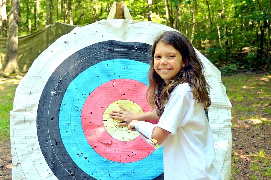 A camper drawing her bow on the archery range