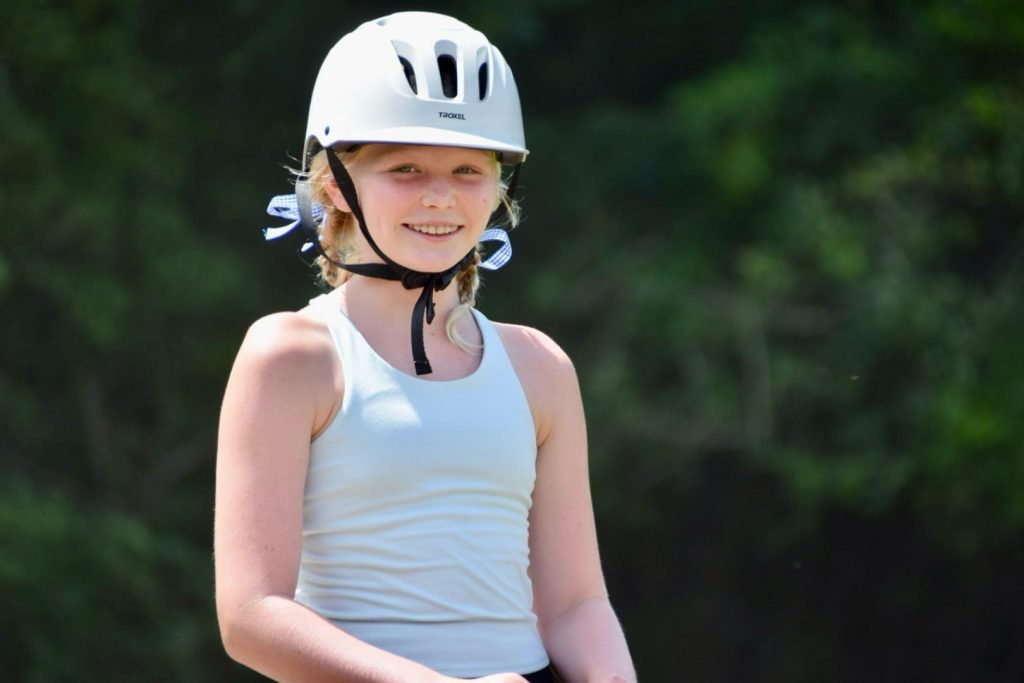 A smiling camper in a riding helmet at the barn