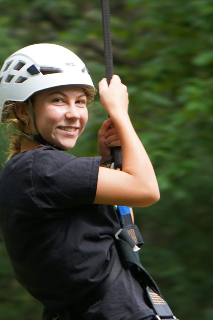 A smiling camper in a helmet and harness on the zip line