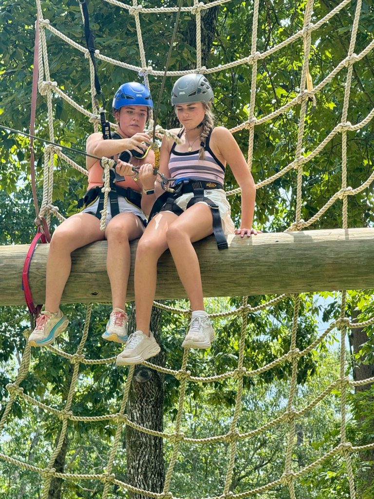 Two campers in helmets on the cargo net of the ropes course