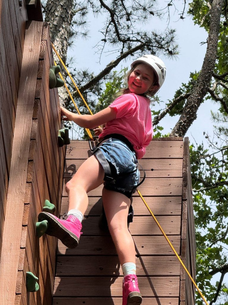 A camper in a helmet climbing the climbing wall
