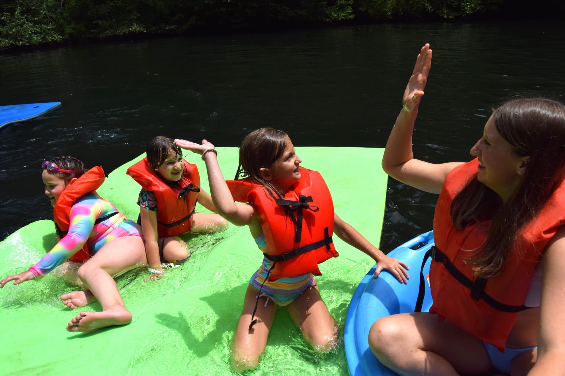 Campers in life jackets on a water float high-fiving their counselor