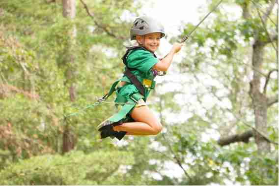 A young camper in a helmet smiling on the zip line