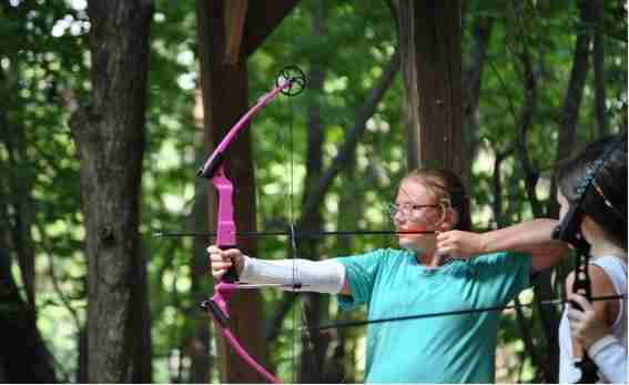 A camper drawing her bow at the archery range